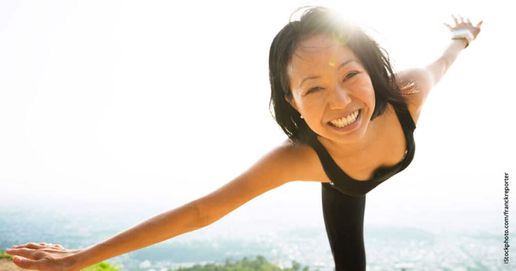 Asian woman grinning while doing yoga outdoors