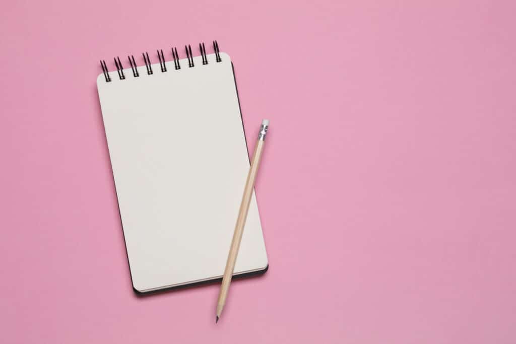 Spiral notebook and pencil isolated on pink background