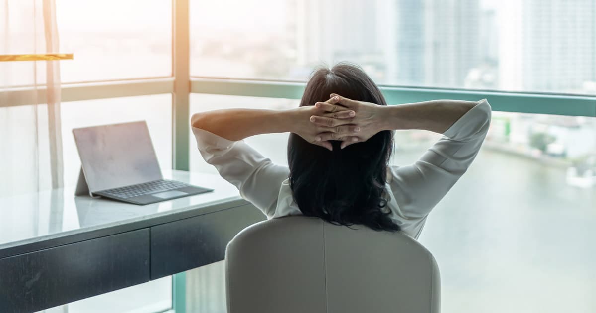 Asian business woman relaxing at desk with arms behind head