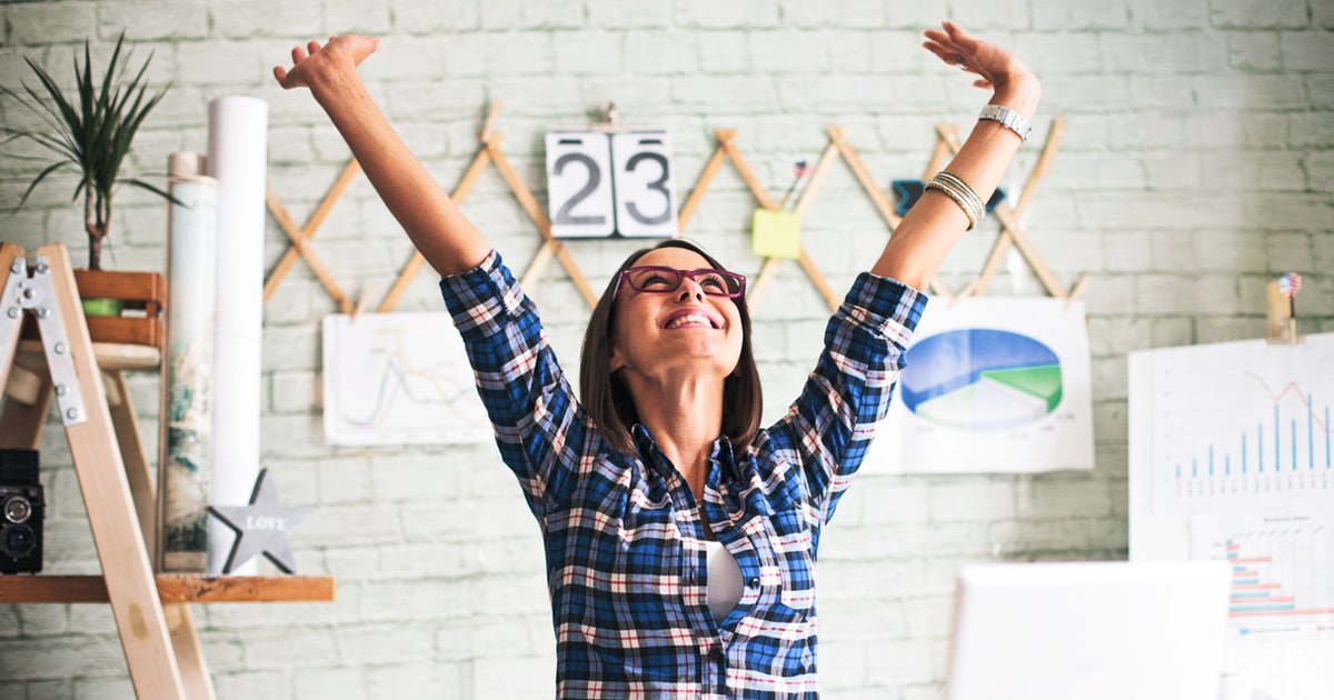 excited, young business woman celebrating success in the office with her arms up in the air